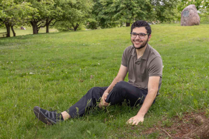 Rutgers student Adnan Alkhalili sits and touches grass near Passion Puddle between the Cook and Douglass campuses.