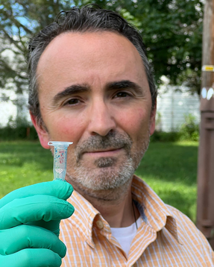 Man wearing green safety gloves holds a small plastic tube
