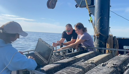 Three people on the deck of a fishing vessel work on an experiment.