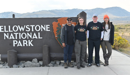 Four scientists stand next to the sign at the entrance of Yellowstone National Park.