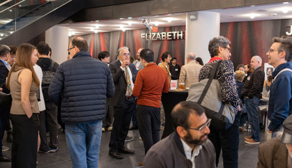 A crowed of people stand around and chat at a celebration.