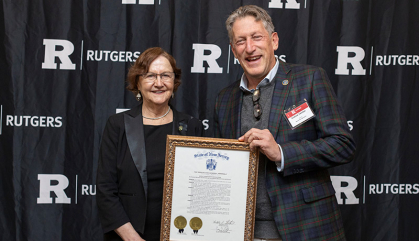 Man and woman stand in front of a black background and hold a proclamation.