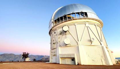 A white building housing a telescope is at right with a pink and blue sky behind.