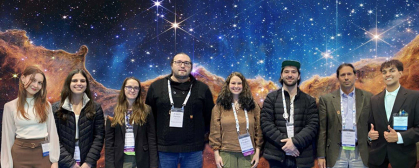 A group of 8 scientists stand before a backdrop of a star poster