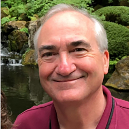 A smiling man outside and wearing a red shirt