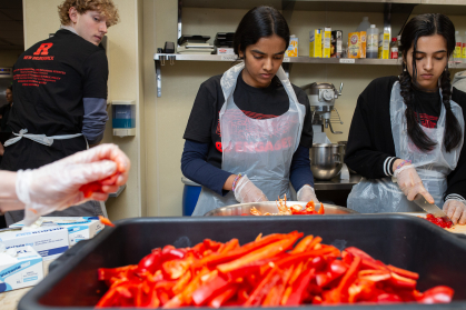 Two students cut red bell peppers in a kitchen