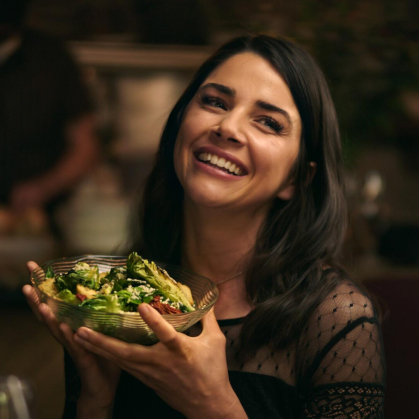 A young woman smiles as she holds up a bowl of salad in a scene from "Love New York."