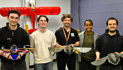 Four students stand with their professor in their lab displaying various experimental robotic birds.