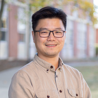Man in tan shirt standing in front of brick building