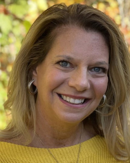 Woman in a gold shirt outside with a tree behind her.