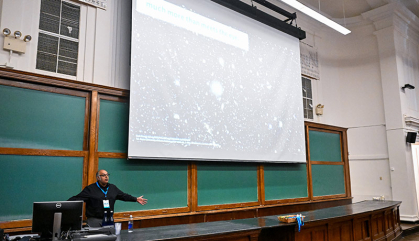 Professor standing below a screen bearing astronomical images.