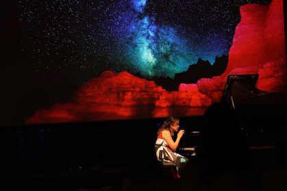 Min Kwon, seated before a piano, performs compositions from "America/Beautiful" during a concert.
