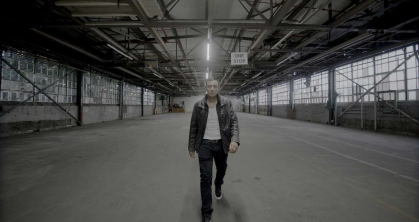 In a scene from "The Muscle," a man wearing a black leather jacket walks through an empty hangar.