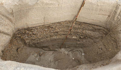 A trench dug on a beach shows layers of sediment.