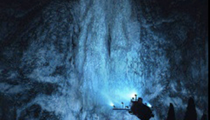 The research submersible Alvin explores the sea floor shining a bright light on a structure out of the deep black.