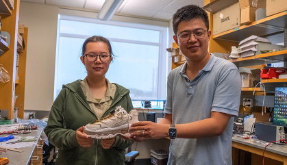 Two people stand in an engineering lab holding a sneaker.