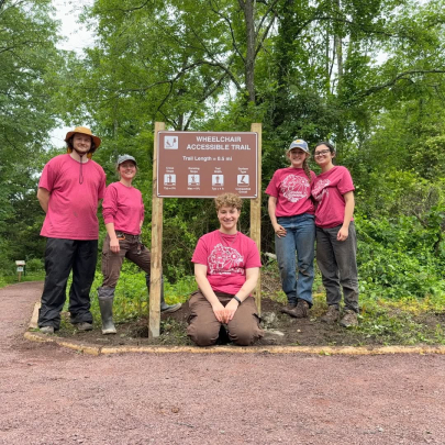 Summer interns at the Rutgers Ecological Preserve in front of a wheelchair accessible trail sign