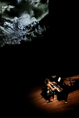 Min Kwon playing piano in front of a backdrop of a large mountain