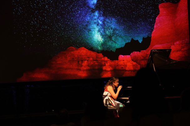 Min Kwon playing piano in front of a backdrop of the night sky over red illuminated mountains