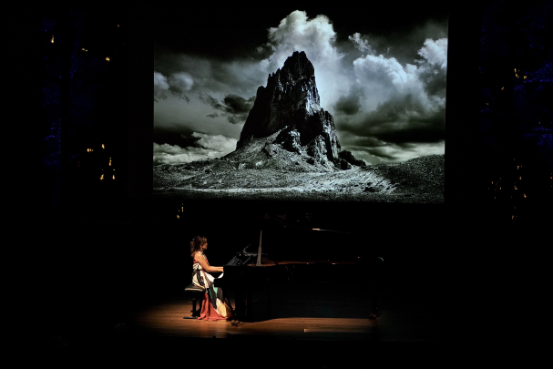 Min Kwon playing piano in front of a backdrop of a large mountain