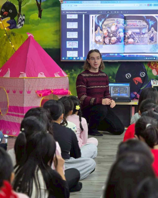Evan Charles Keeton discusses a page from the children's book "Who's That Knocking on Christmas Eve?" with young students in the library of an elementary school.