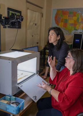Lena Struwe (right), director of the Chrysler Herbarium, shows Sue Huang a lightbox and camera setup used to digitize plant specimens.