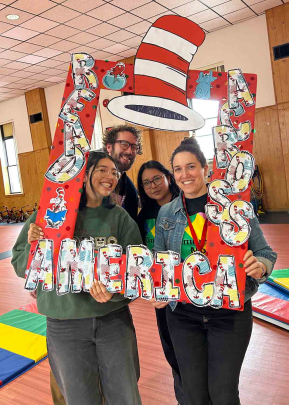 Three woman and a man pose behind a handmade frame that reads "Read Across America."