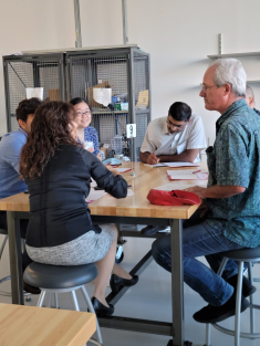 People seated around a wooden table in a room with metal shelves, engaged in discussion at a networking event
